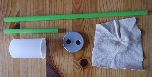 Two straws, a film canister with two holes in the lid, and a piece of cloth